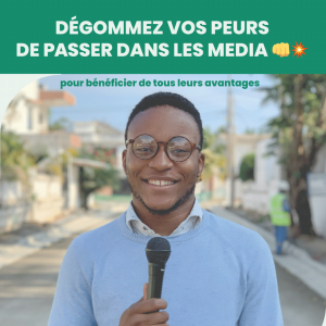 Jeune homme souriant portant lunettes rondes et pull bleu clair tient un micro, prêt à oser passer dans les media en extérieur ensoleillé